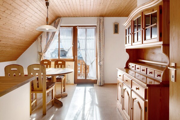 A wooden interior with a dining table, chairs, a cabinet, and a window with curtains.