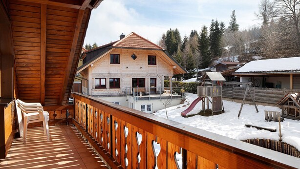 A wooden balcony with chairs, a snow-covered yard, and a house with a red roof. - Apartment 'Weideglück' with Shared Garden, Balcony and Wi-Fi (Feldberg-Altglashütten)