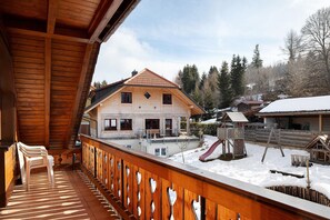 A wooden balcony with chairs, a snow-covered yard, and a house with a red roof.