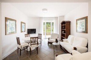 Ein Wohnzimmer mit einem weißen Sofa, einem Esstisch mit Stühlen, einem Fernseher und einem Bücherregal.