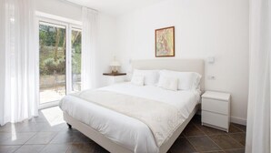 A bedroom with a large bed, a bedside table, a nightstand, and a window with curtains. - Glicine- 03 bedroom apartment with private terrace (Massa Lubrense)