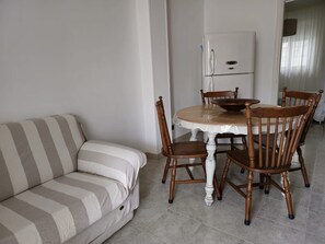 Olohuoneessa on raidallinen sohva, pyöreä ruokapöytä tuoleineen ja valkoinen jääkaappi.