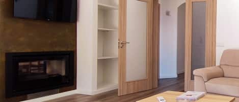 Una sala de estar moderna con un televisor de pantalla plana montado en la pared, una mesa de centro de madera, un sofá color beige y una estantería.