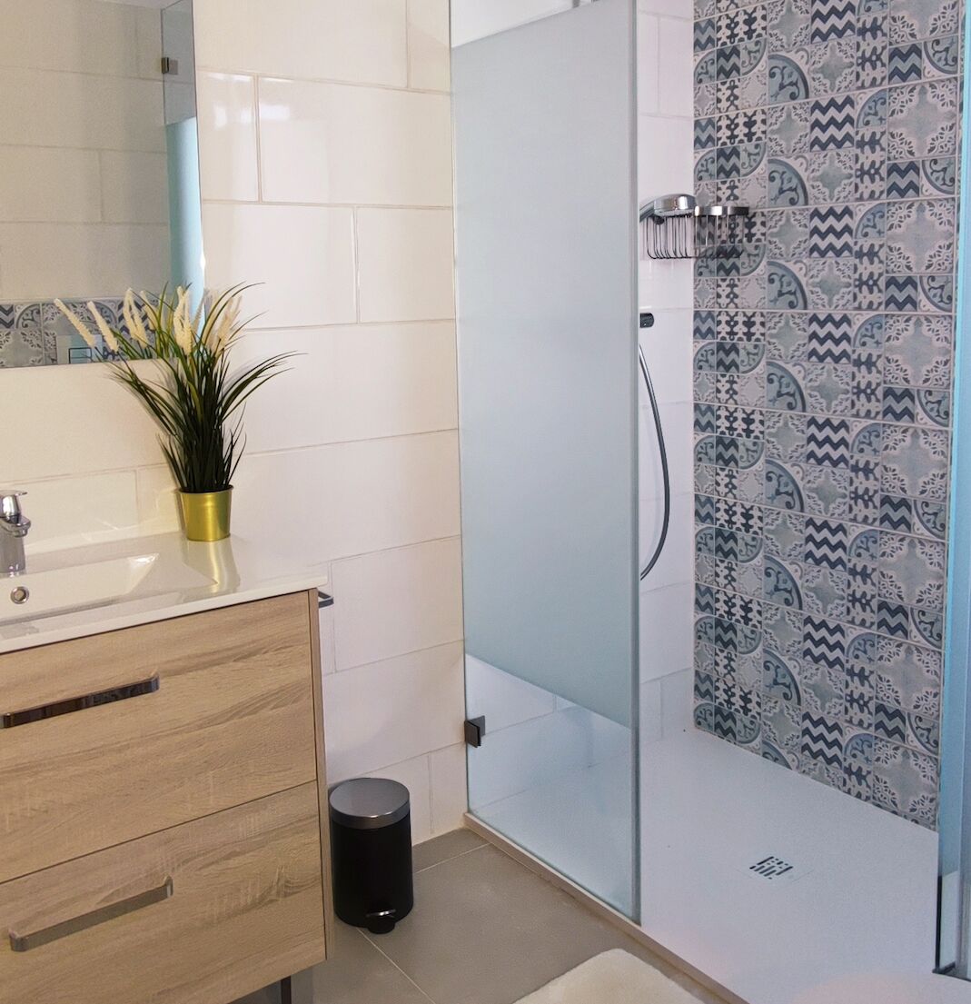 A bathroom with a white sink, wooden cabinet, and a glass shower enclosure with patterned tiles.