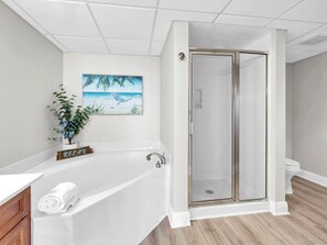 A modern bathroom with a bathtub, a glass shower enclosure, a potted plant, and a beach-themed painting on the wall. - 🏝️BEACH FRONT | Gulf Views | Great Amenities | Emerald Beach 1831🏝️ (Panama City Beach)