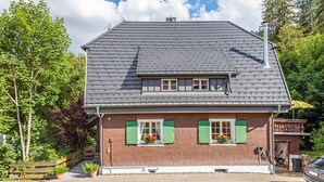 Une maison à deux étages avec un toit recouvert de tuiles grises, des volets verts et une façade en briques.