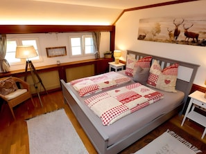 Ein Schlafzimmer mit einem Bett, einem Sessel, einer Lampe, einem Bild an der Wand und einem Fenster.