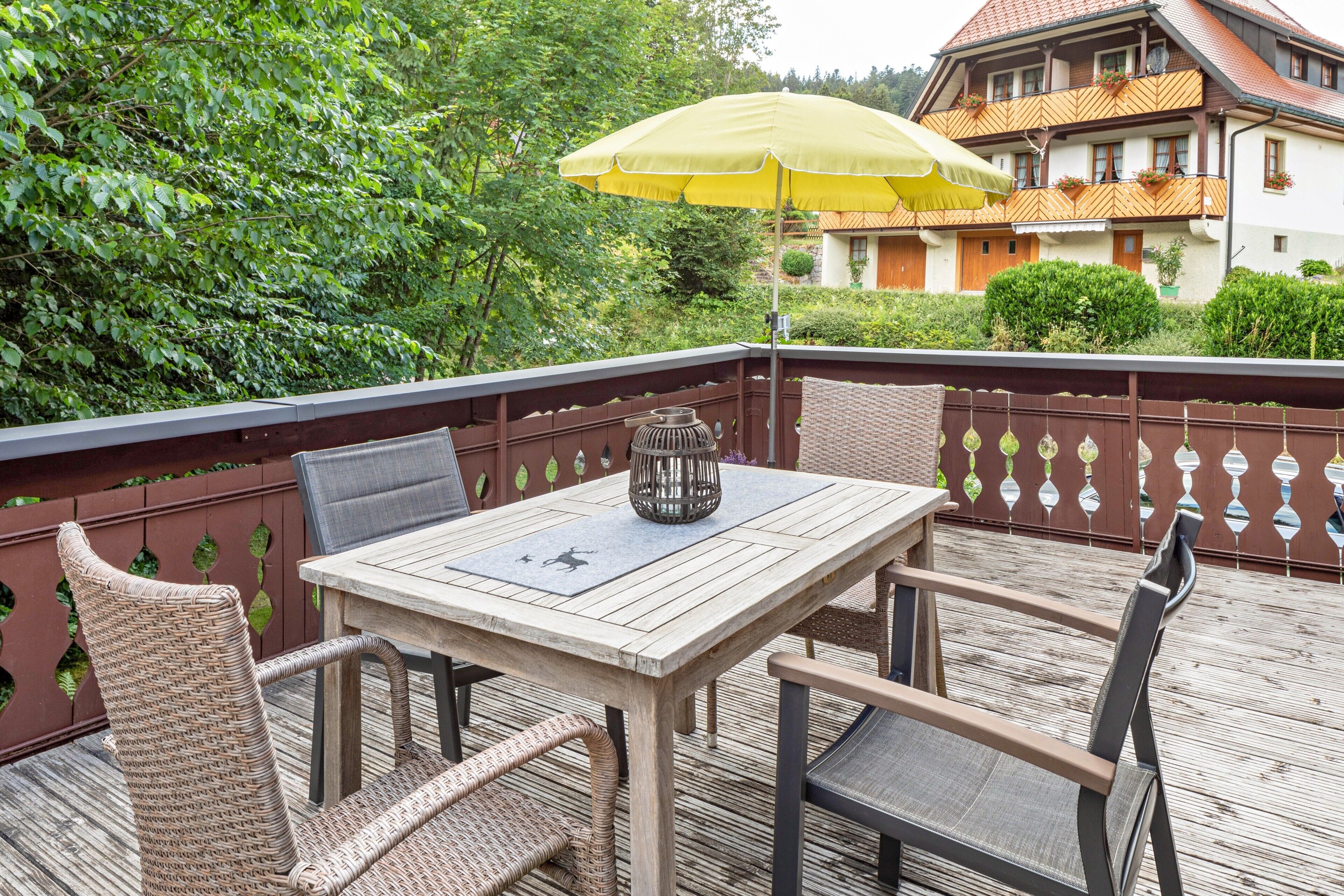 A wooden deck with a table and chairs, a yellow umbrella, and a view of a building with balconies.