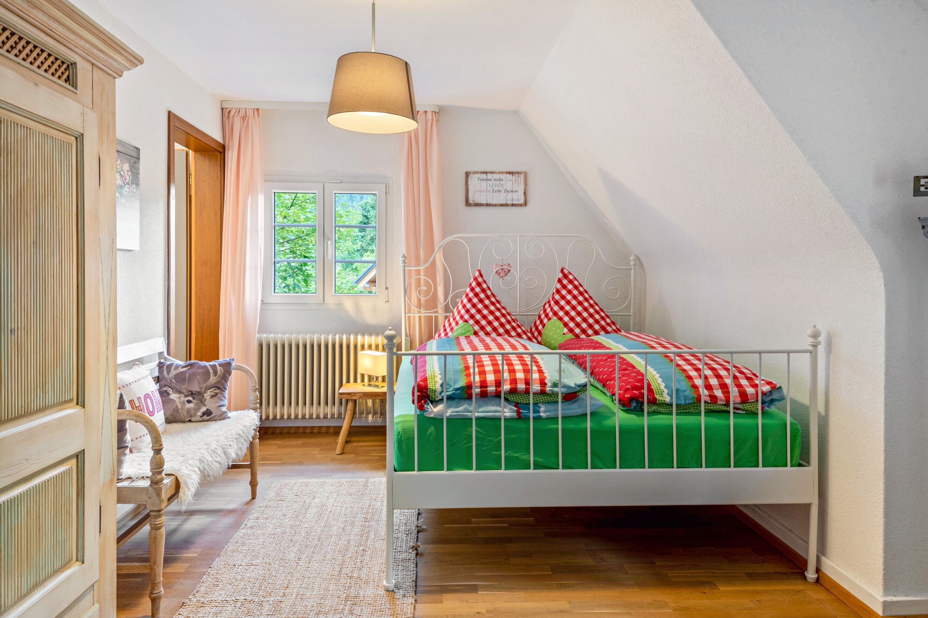 Ein Schlafzimmer mit Bett, Fenster, Heizkörper, Stuhl und einer Pendelleuchte.