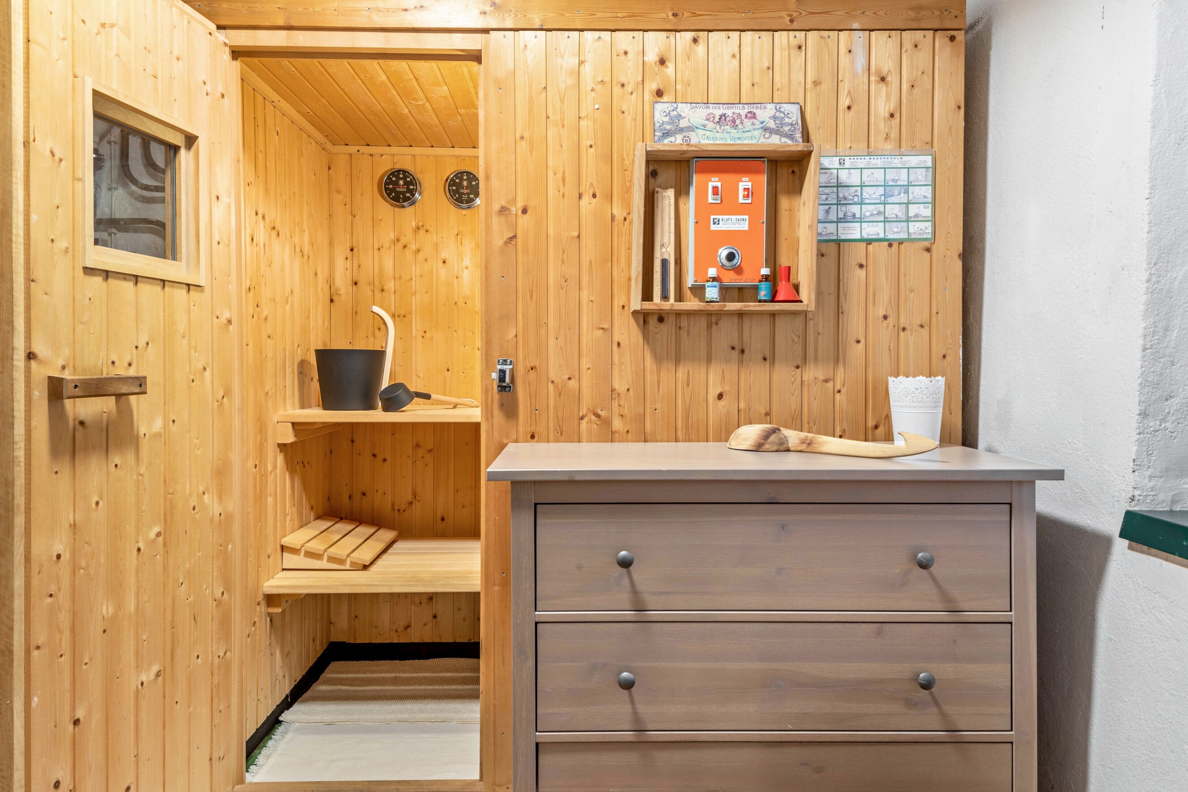 Een sauna met houten wanden, een houten bank, een bedieningspaneel en een klein plankje met spullen.