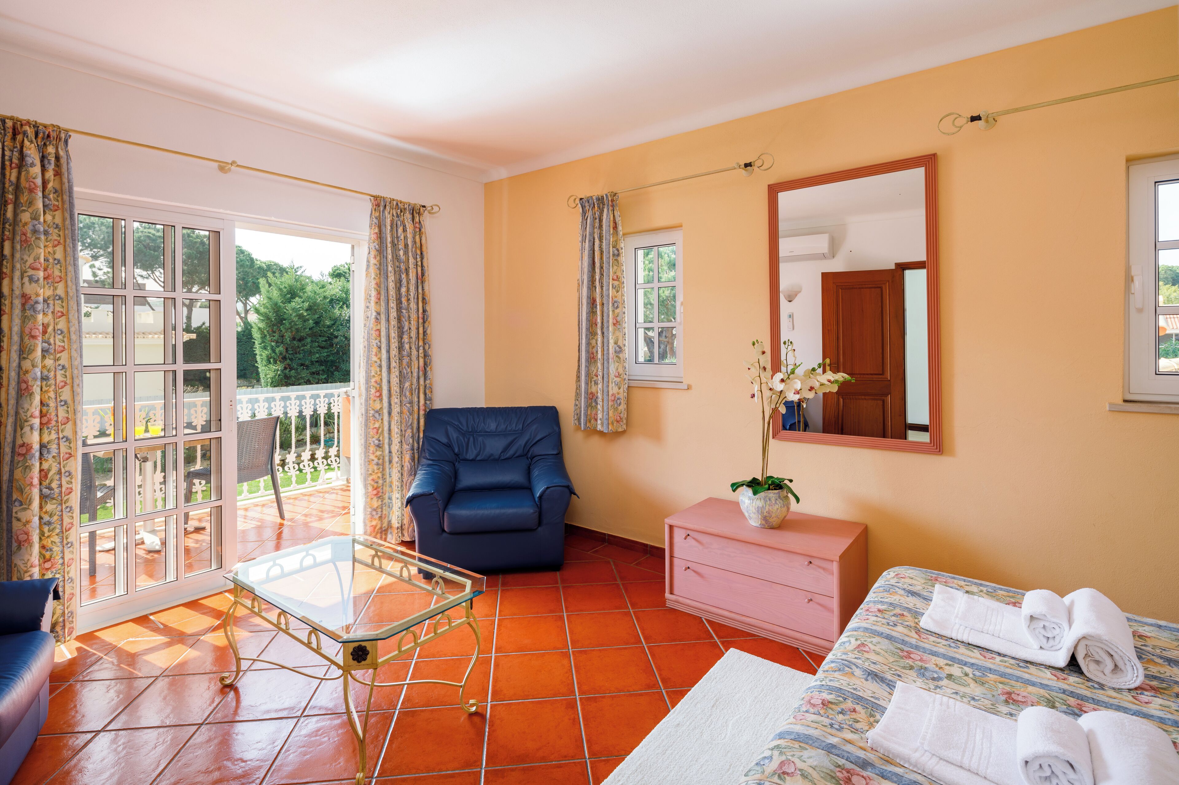 A room with a balcony, a sofa, a chair, a bed, a dresser, and a mirror.