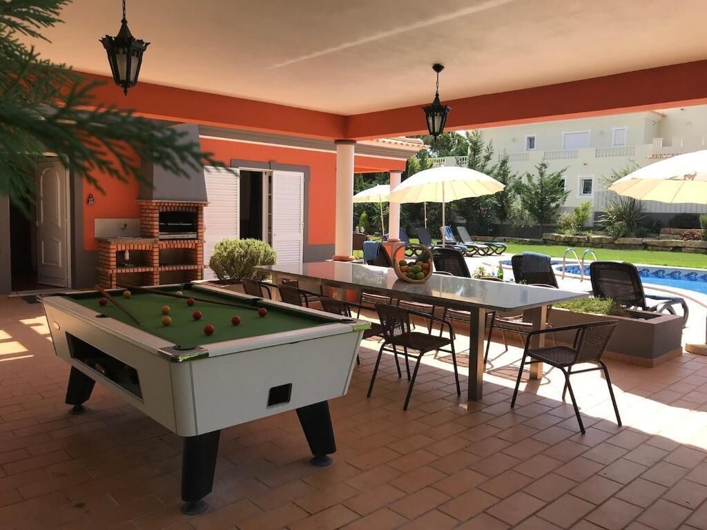 A pool table with a green felt surface, surrounded by outdoor seating with umbrellas.