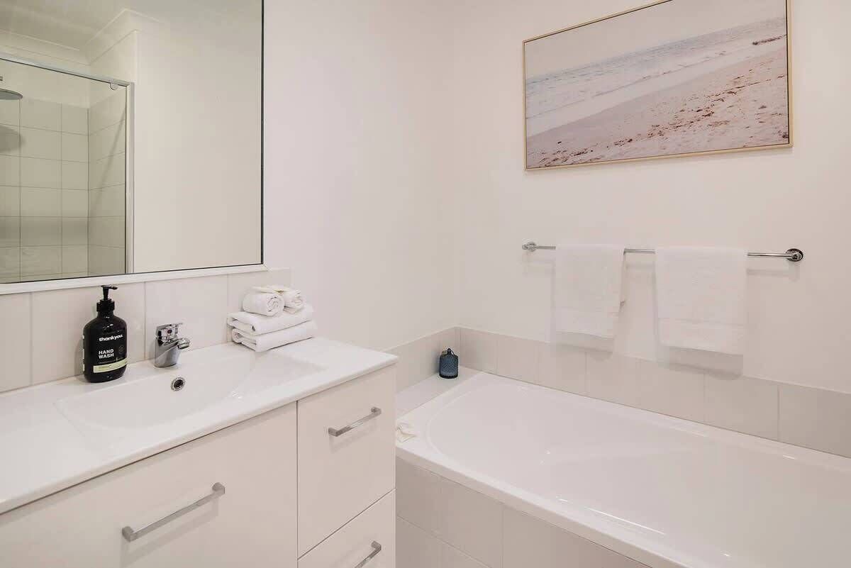 Ein Badezimmer mit einer Badewanne, einem Waschbecken, einem Spiegel und einem gerahmten Bild an der Wand.