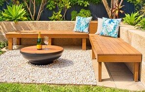 An outdoor seating area with a round table, benches, and a small fire pit. - Peaceful Garden Hideaway—Swim, Hike & Unwind (Dunsborough)