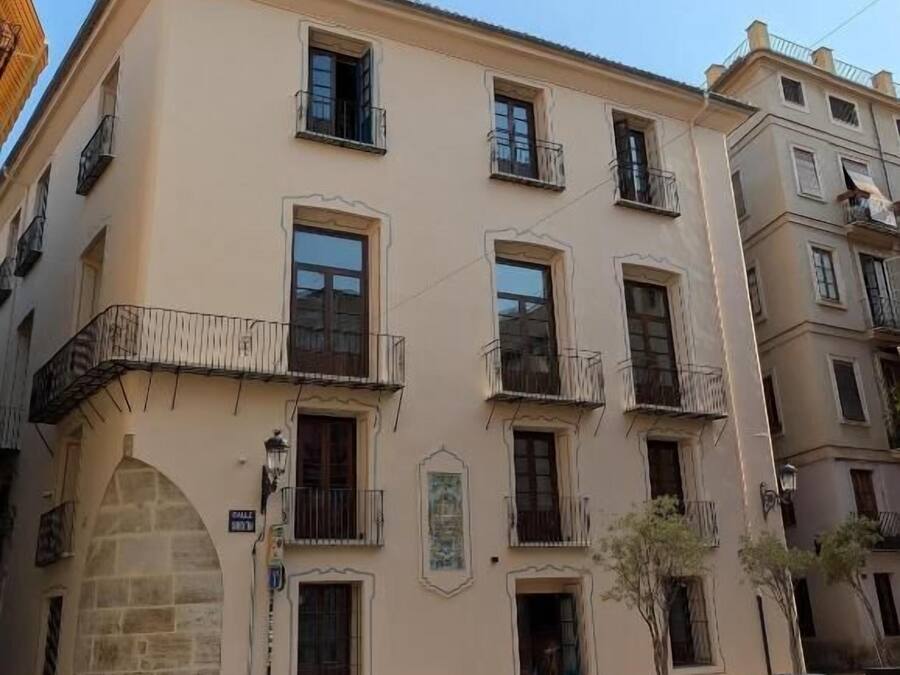 Un immeuble à plusieurs étages doté de balcons, d’une arche en pierre et bordé d’une rue.