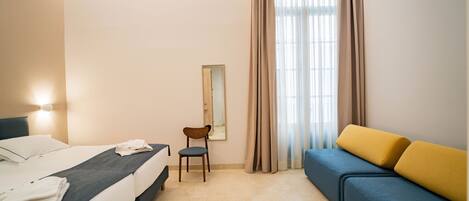 A hotel room with a bed, a chair, a sofa, and a mirror.