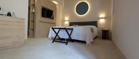Un dormitorio con cama, una lámpara redonda fijada a la pared, techo de madera y suelo de baldosas.