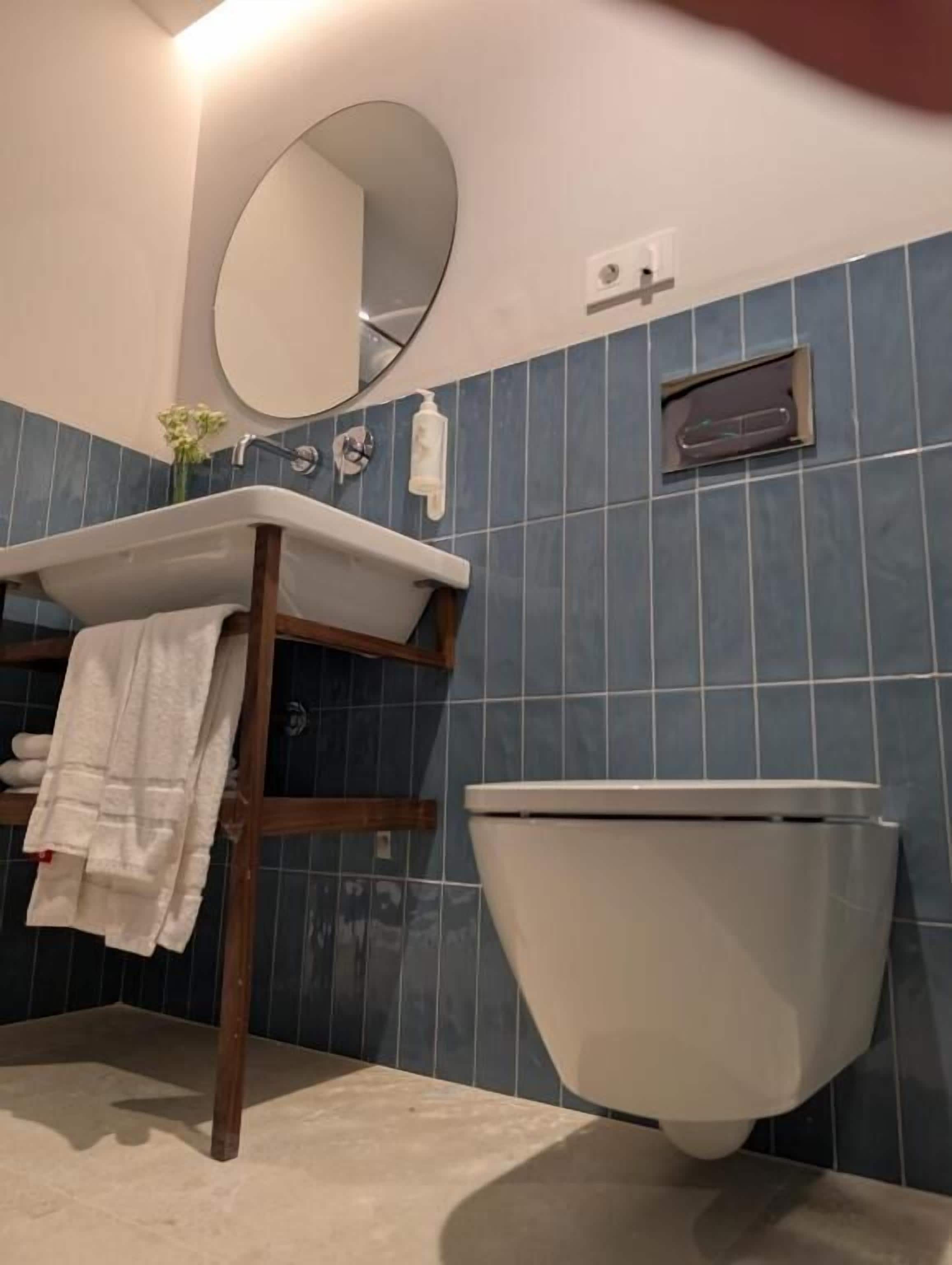 A bathroom with a white sink, a mirror, a toilet, and blue-tiled walls.