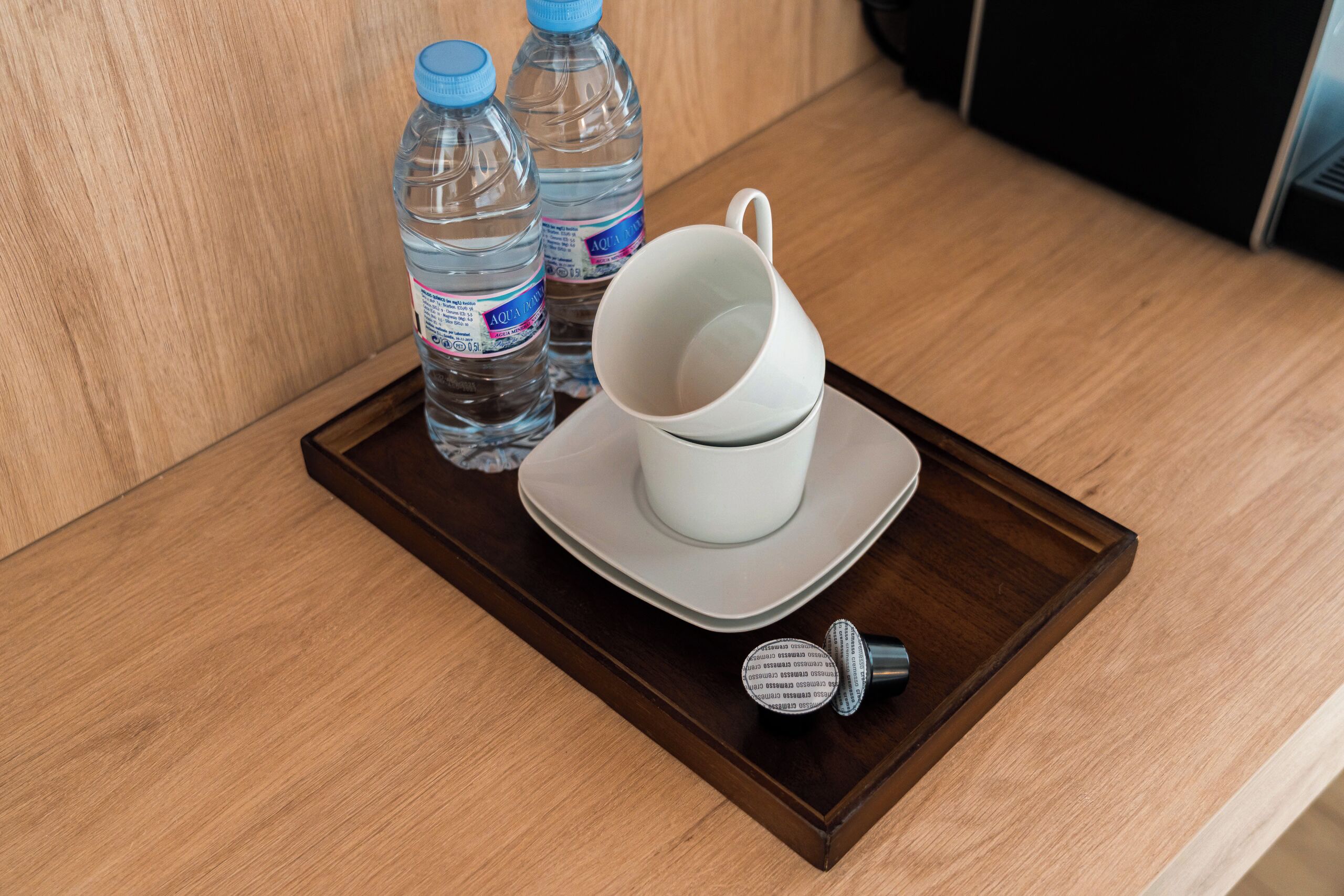 A tray with two water bottles, a white mug, and a white cup on a wooden table.