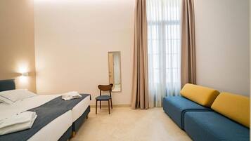 A hotel room with a bed, a chair, a sofa, and a window with curtains.