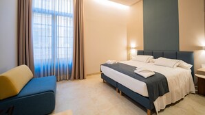 A modern hotel room with a bed, a blue sofa, and a large window with curtains.