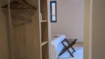 Een kamer met een houten garderobe, een bed met een witte dekbedovertrek en een droogrek.