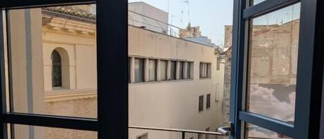 A view from a balcony with a metal railing, overlooking a row of buildings with flat roofs and multiple windows.