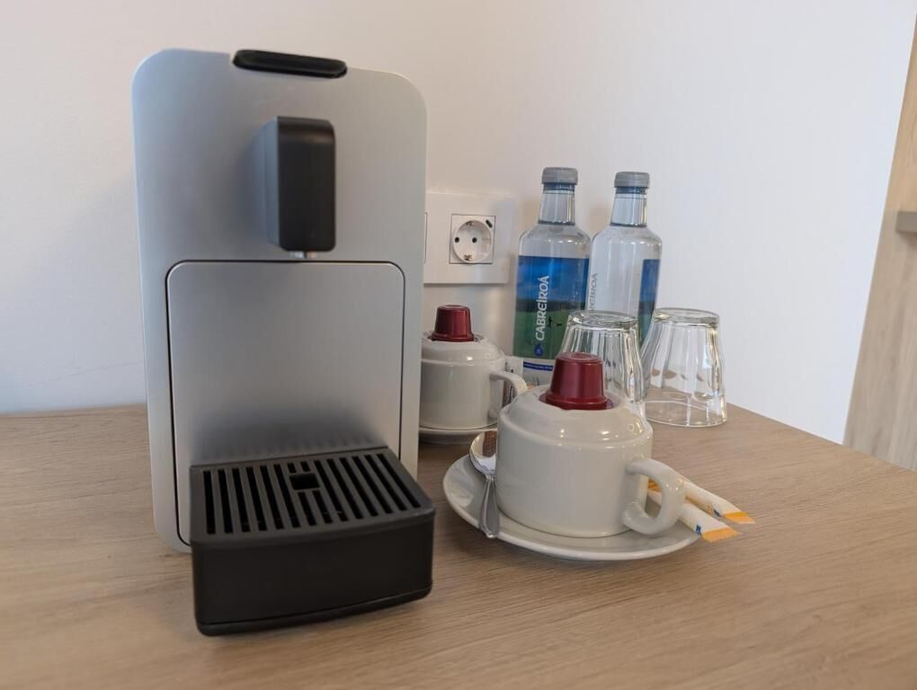 A coffee maker, two bottles of water, a red mug, and two clear glasses on a wooden table.