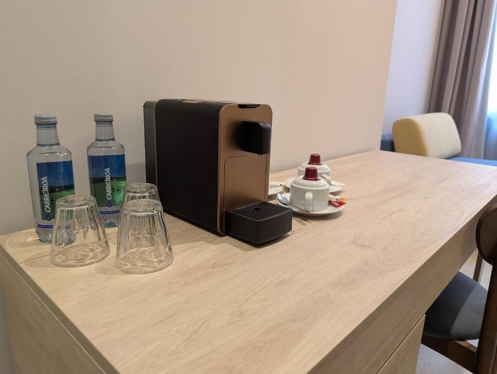 Ett hotellrum med ett skrivbord i trä, en kaffemaskin, två flaskor vatten och en kopp kaffe.