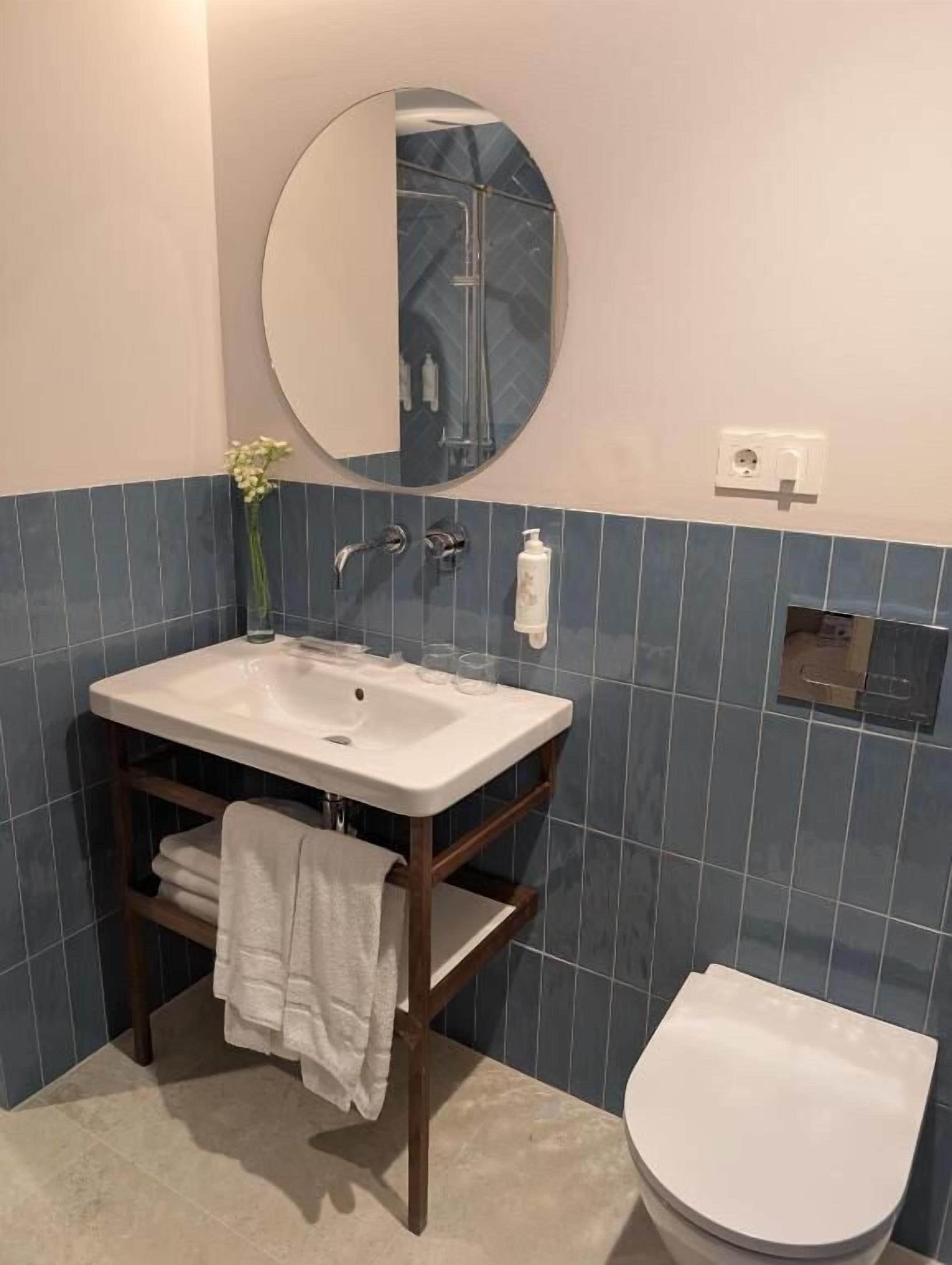 A bathroom with a white sink, a mirror, a toilet, and blue-tiled walls.