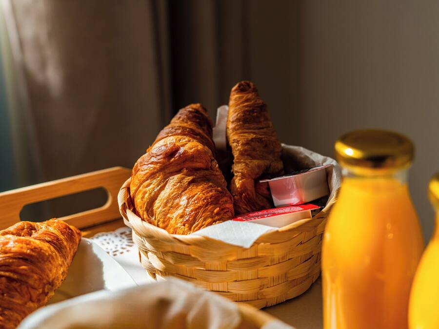 A basket of croissants and a bottle of orange juice on a tray.