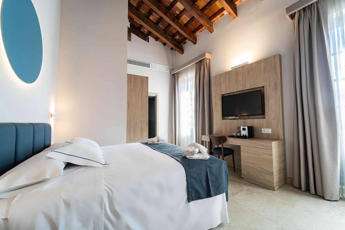 Une chambre d’hôtel équipée d’un lit, d’un bureau, d’une télévision et d’une grande fenêtre avec des rideaux.