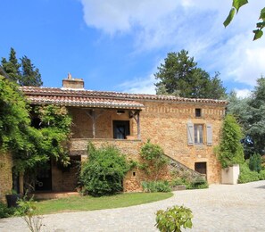 Une maison en pierre avec un toit en tuiles, un porche couvert et une allée pavée.