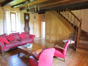 Une pièce avec un escalier en bois, un canapé avec des coussins rouges, une table basse en bois et un fauteuil.
