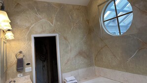 Une salle de bain avec un mur en marbre, une lucarne, une baignoire et un meuble-lavabo doté d’un miroir et d’un éclairage.