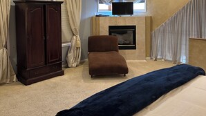 Une chambre à coucher comprenant un lit, une chaise, une armoire, un ventilateur de plafond et une cheminée.