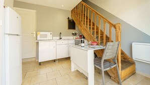 A compact kitchen with white cabinets, a wooden staircase, and a dining area with a chair. - Cottage with Private Spa and Pool (Pont-de-l'Isère)