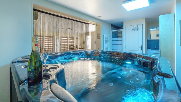A hot tub with a bottle and glass, a ceiling light, and a door with a towel rack. - Cottage with Private Spa and Pool (Pont-de-l'Isère)