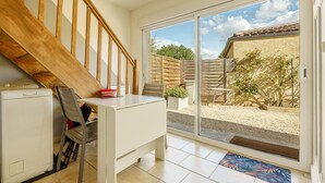 A room with a wooden staircase, a white desk, a chair, a small white appliance, and a sliding glass door leading to an outdoor area with a patio and a garden. - Cottage with Private Spa and Pool (Pont-de-l'Isère)