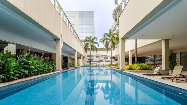 Una piscina interior moderna con paredes de azulejos y agua azul cristalina, rodeada de sillones de descanso y follaje.