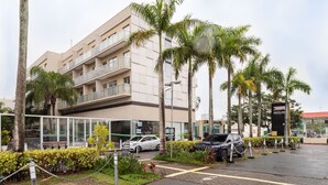 Un edificio moderno con fachada plana, varios balcones y un estacionamiento con coches.