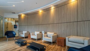 Un área de espera moderna con paneles de madera, varios sillones blancos, una mesa baja negra y un sofá azul.