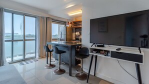 Una cocina moderna con una isla grande, taburetes de bar, un televisor de pantalla plana y vistas a una masa de agua a través de amplios ventanales.