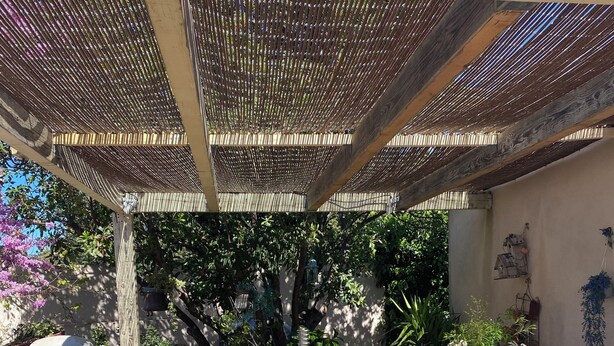 A covered patio area with a table and chairs, surrounded by potted plants and a wooden fence.