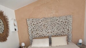 A bedroom with a large bed, a decorative headboard, bedside lamps, a wall clock, and a woven wall decoration.