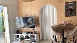A modern living room with a TV, wicker pendant lights, a dining table, and a cozy sofa.