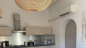 A modern kitchen with a gas stove, oven, and a coffee machine. There is a dining area with a white table and chairs.