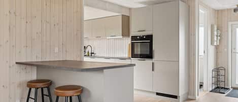 A modern kitchen with a central island, bar stools, and a built-in oven.