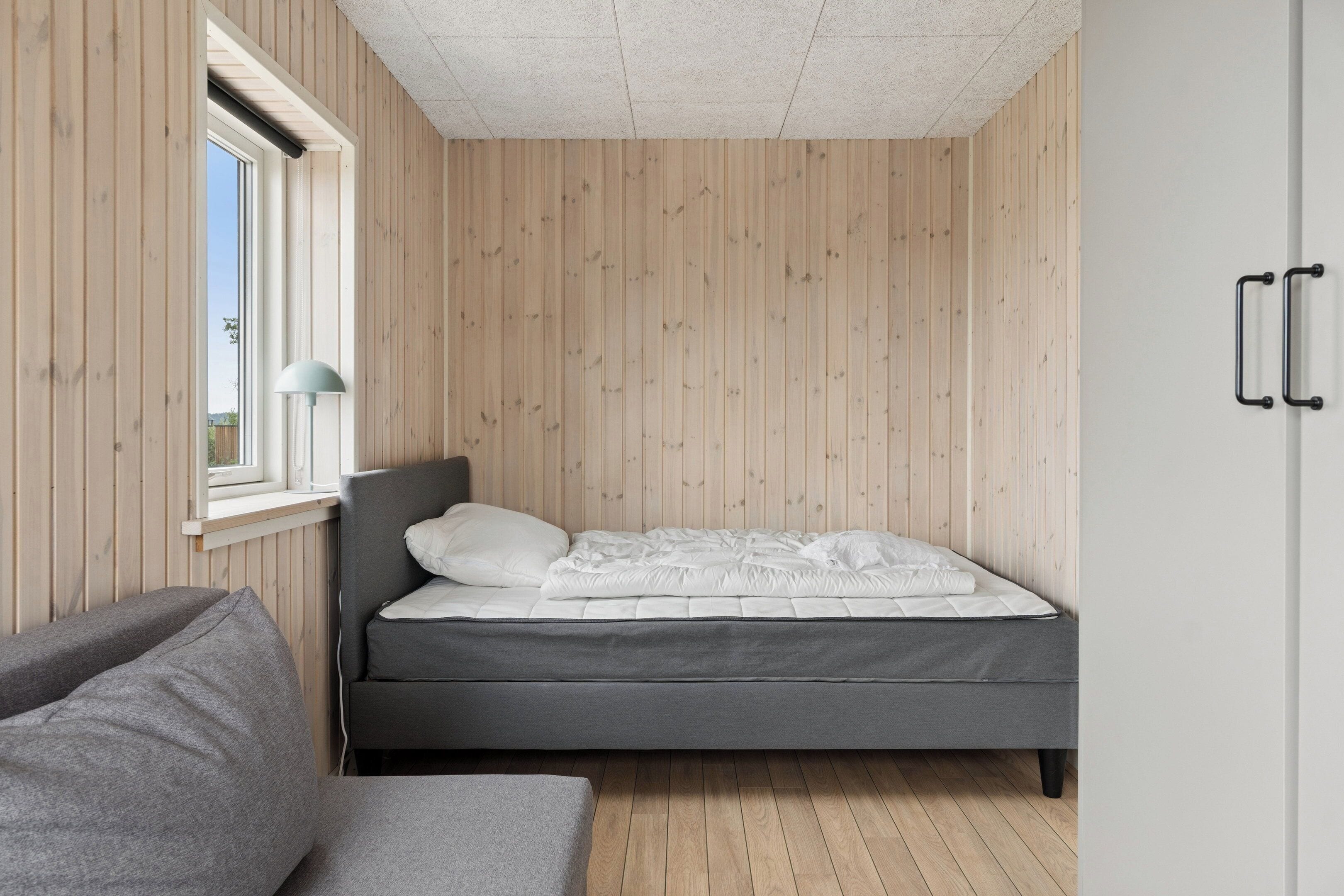 Une chambre à coucher avec un lit, une fenêtre, une lampe et des murs en bois.
