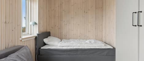 A bedroom with a bed, a window, a lamp, and wooden walls.
